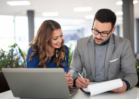 Dos personas trabajando juntas en una oficina con un portátil y documentos.
