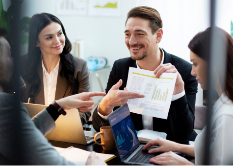 Hombre en reunión de oficina mostrando un informe con gráficos a sus compañeros.