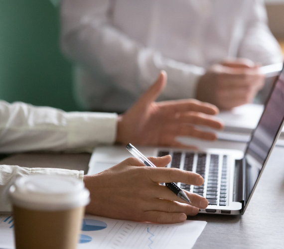 Personas en una reunión de trabajo con portátil, documentos y una taza de café.